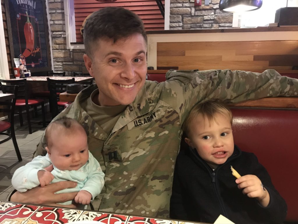 a military dad sits with his two kids in a booth at a restaurant.