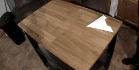 gif of a paper airplane being blown across a table