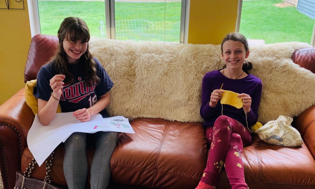 two girls crocheting and sewing at home