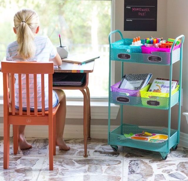 a girl does her homework with supplies on a cart on wheels nearby