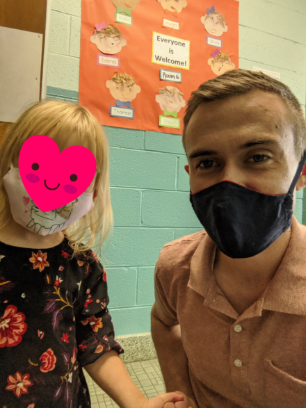 a father drops his daughter off at daycare while wearing masks