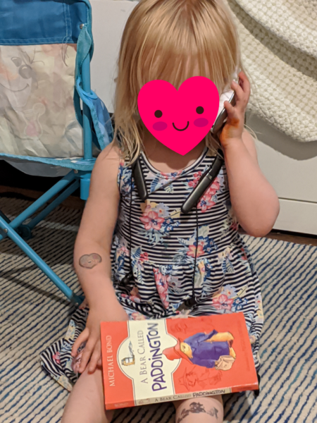 a toddler pretends to be on the phone while reading a book