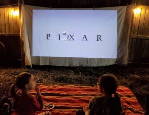 Two young girls watch a Pixar movie in their backyard on a projector.