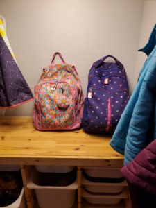 Two backpacks sit ready on the bench in a family's entryway.