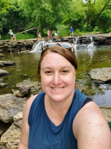 A woman takes a selfie alongside a river in the summertime.