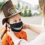 Mother putting protective face mask on her child during COVID-19 pandemic on Halloween