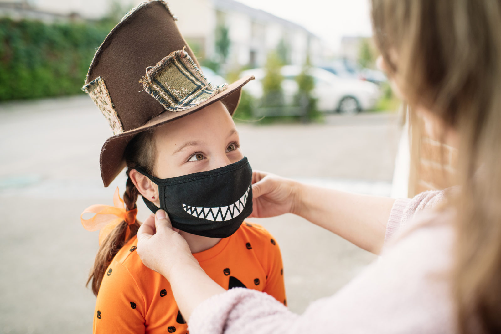 Mother putting protective face mask on her child during COVID-19 pandemic on Halloween
