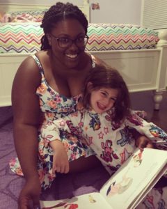 A woman and young girl read a book at home.