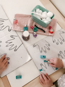 Kids practicing to paint their nails on a cardboard drawing.