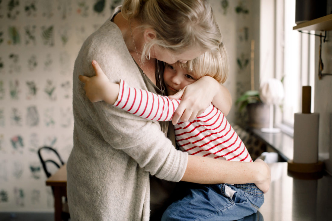 A woman hugs a child in the kitchen.