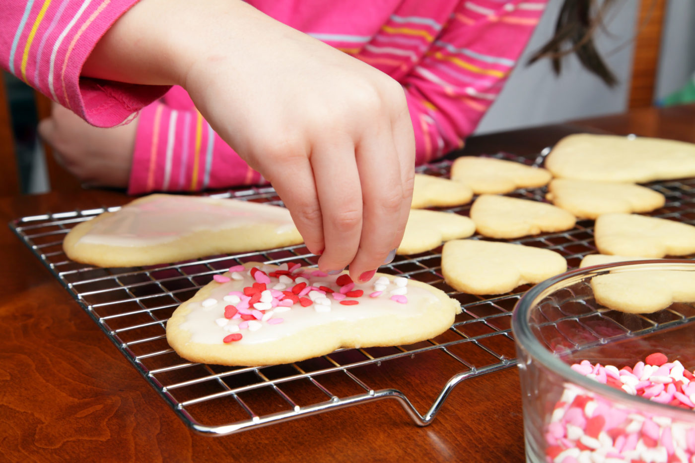 A young girl adds heart sprinkles to her Valentine's cookies.