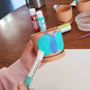 A child paints a butterfly on the side of a terra cotta pot.