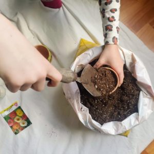 A child fills a terra cotta pot with dirt and seeds.