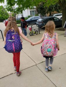 Two girls walk into school with backpacks on.