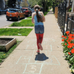 A girl plays hopscotch on the sidwalk.