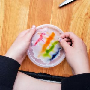 A child peels colorful dried glue off of a plastic lid