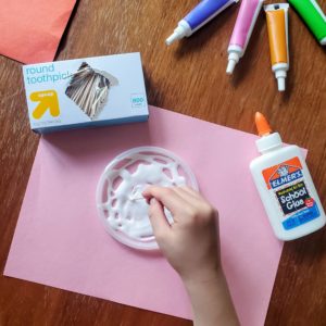 A child spreads glue on a plastic lid with a toothpick